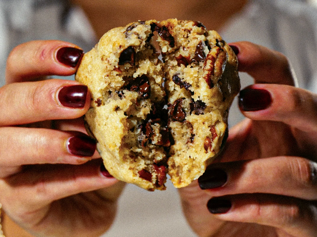 Manos sostienen una galleta abierta con trozos de chocolate.
