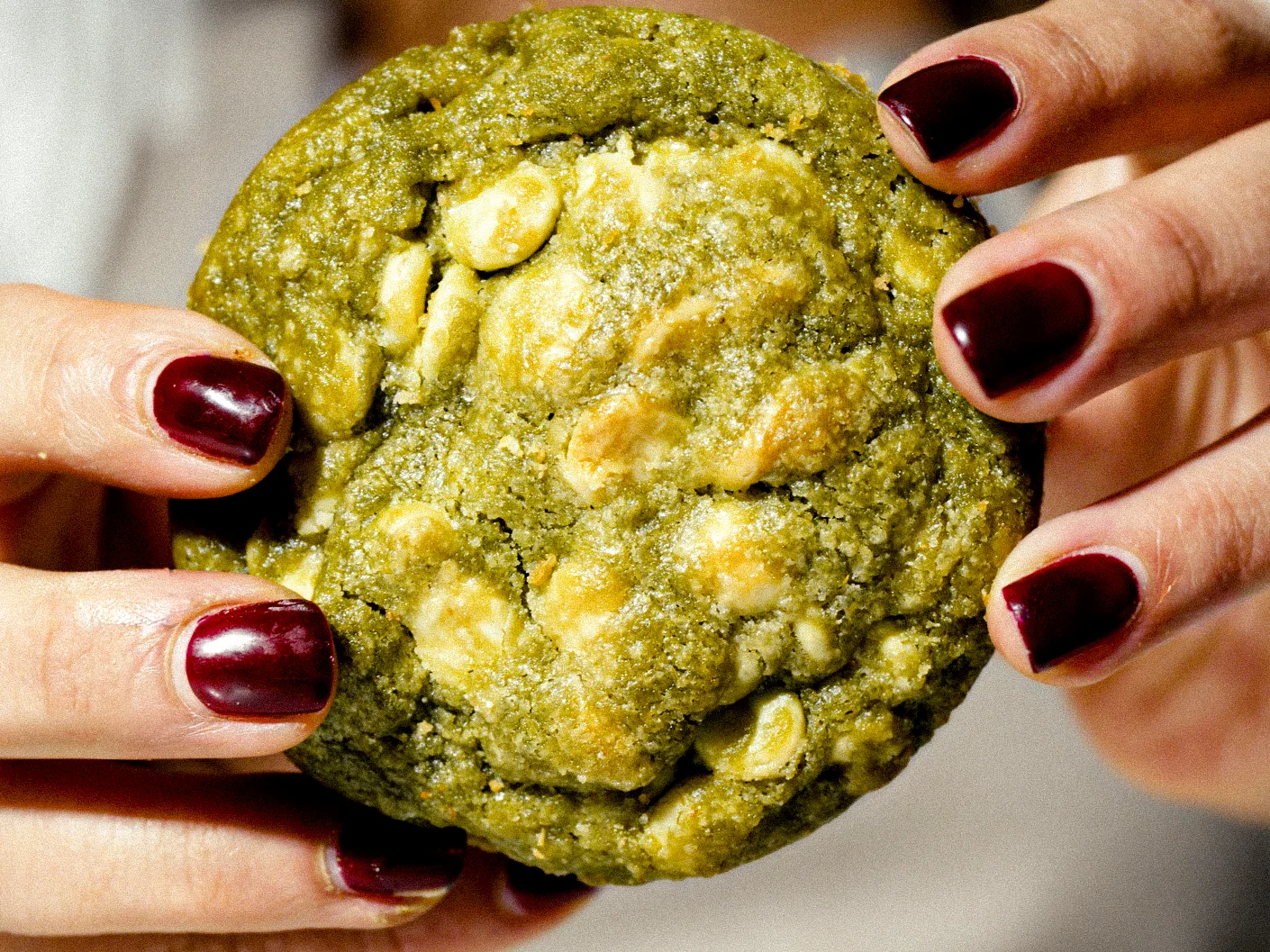 Manos con uñas oscuras sostienen una galleta verde.