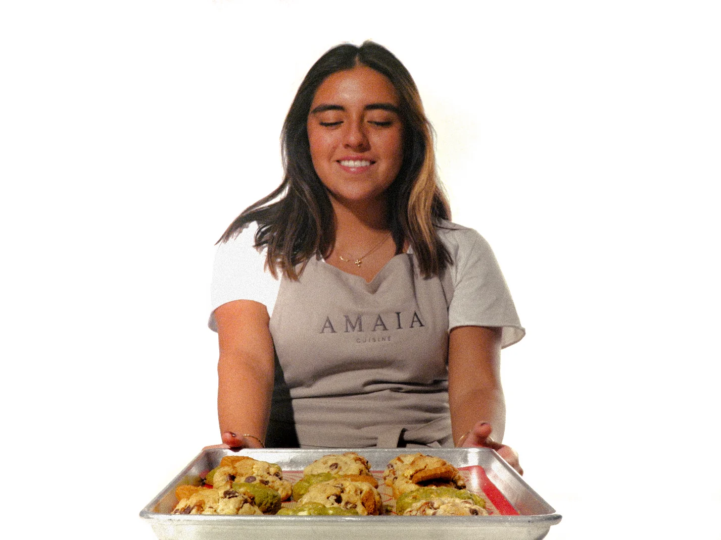 Mujer con delantal gris sostiene una bandeja de galletas.