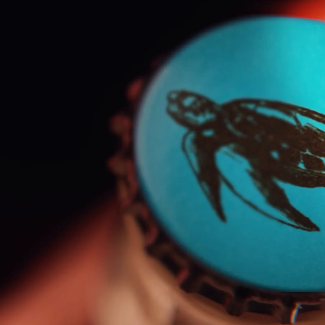 Primer plano de la chapa turquesa de Cerveza Tulum con el logotipo negro de la tortuga.