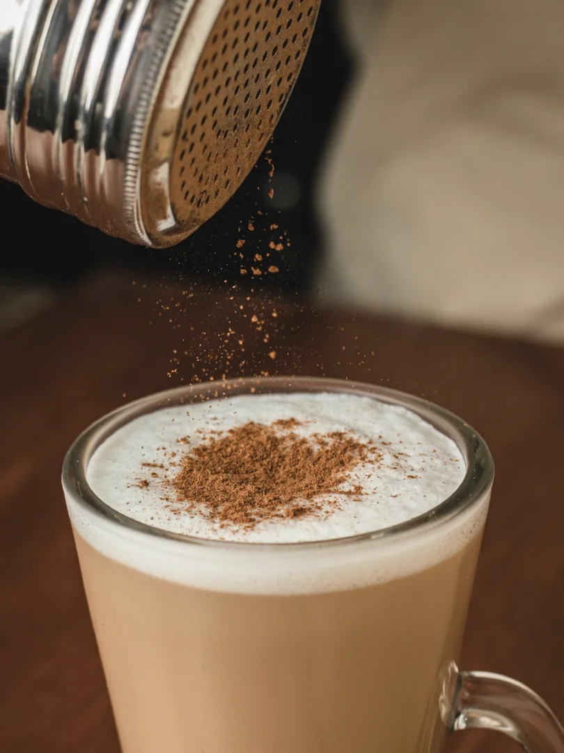 Canela cayendo sobre la espuma de un café con leche.